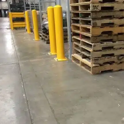 Yellow bollards inside a warehouse in front a row of empty stacked pallets