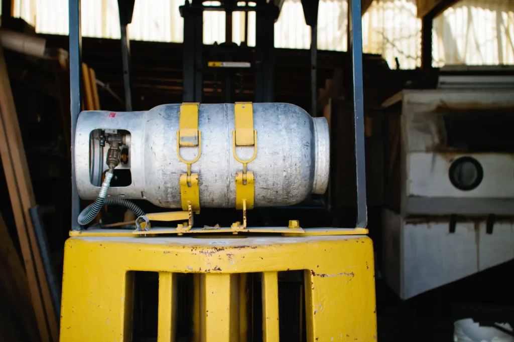 A propane tank on the back of a yellow forklift in a warehouse yard.